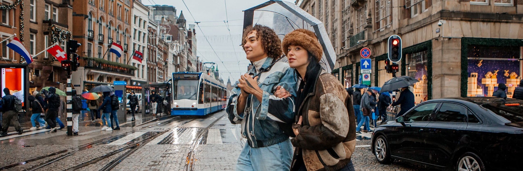 Twee jonge mensen lopen onder een paraplu in het drukke stadscentrum van Amsterdam