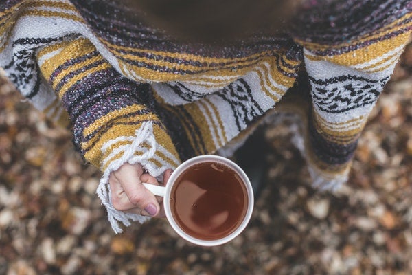 Woman holding tea cup standing in leaves