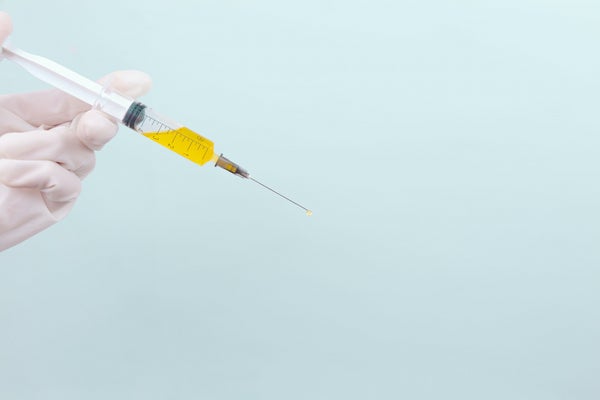 Gloved hand prepared syringe of yellow fluid against plain background
