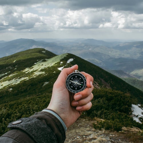 A hiker's hand holding a compass in the mountains