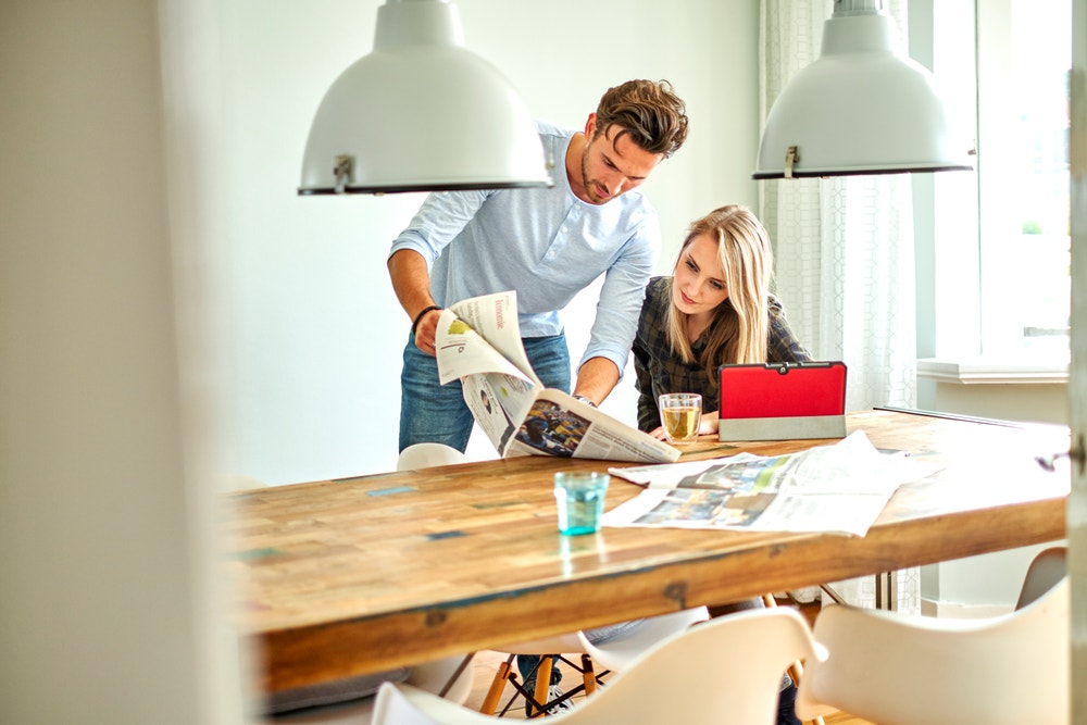 man en vrouw aan tafel met krant een tablet