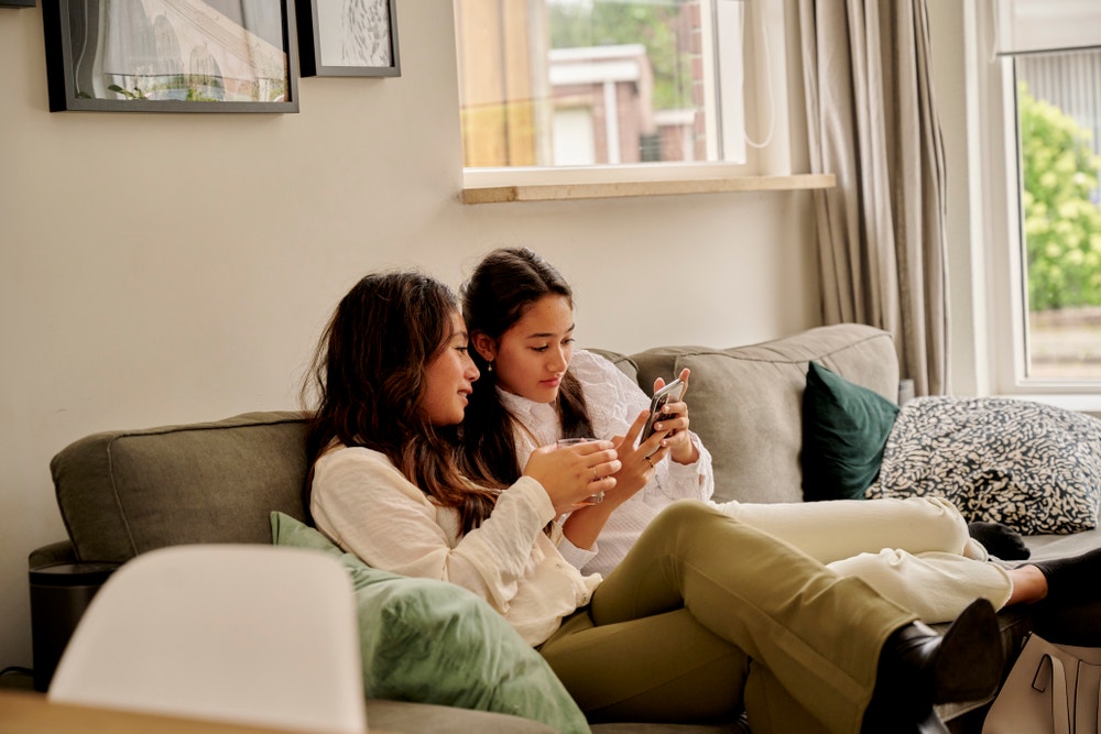 moeder en dochter op bank achter telefoon
