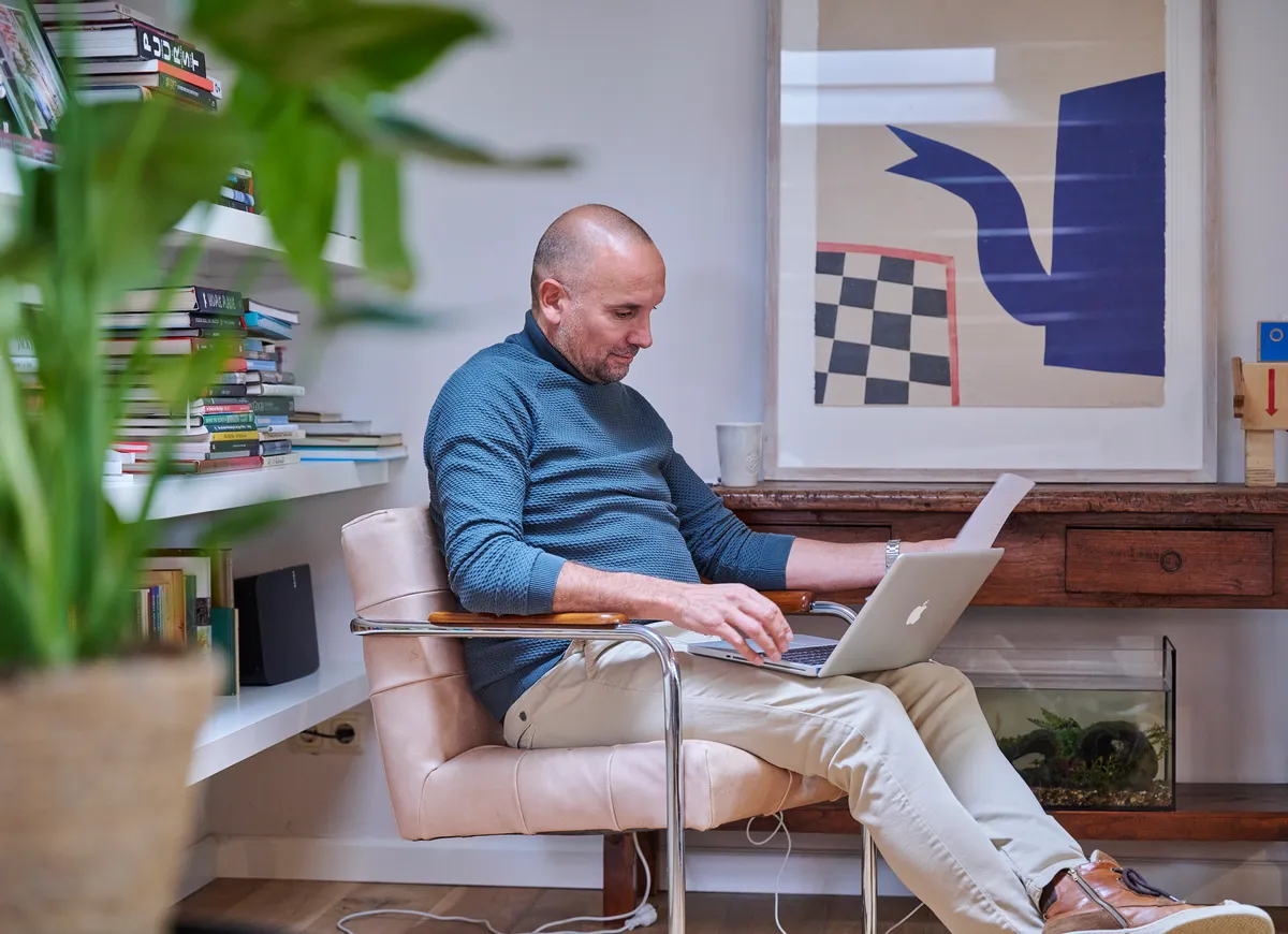 man zit met laptop en papierwerk
