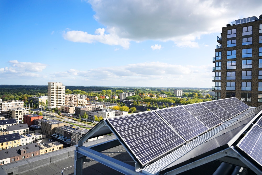 Rij zonnepanelen op plat dak van een hoog appartementencomplex met uitzicht over de stad
