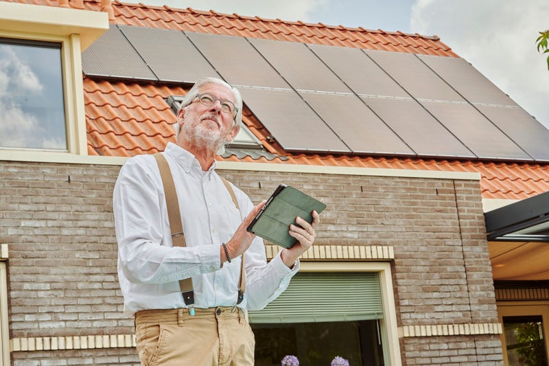 man met tablet voor zijn huis met zonnepanelen