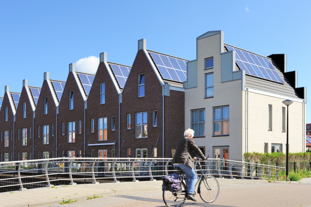 Man fietst langs huizen met zonnepanelen