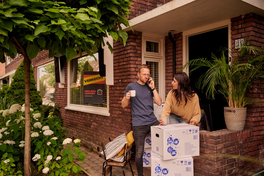 man bellend voor huis met vrouw en verhuisdozen