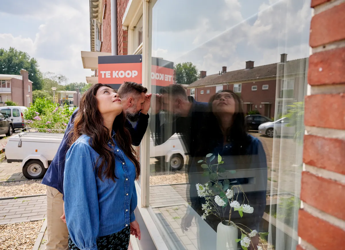 man en vrouw kijken door raam van koophuis