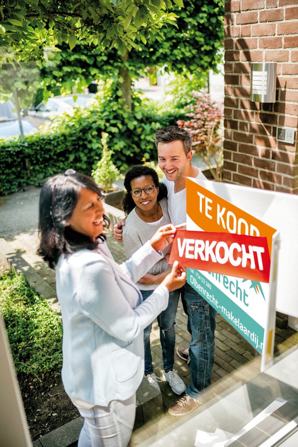 blije mensen staan bij een 'verkocht' bord