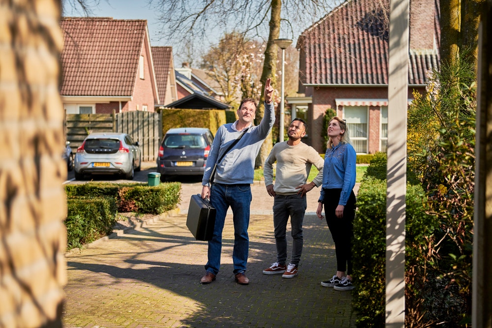 Een man met koffer die wijst, een man en een vrouw lopen door een woonwijk