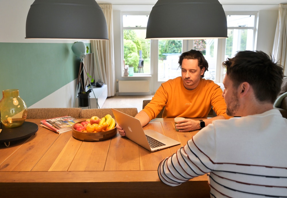 twee mannen zitten aan tafel en kijken naar laptop