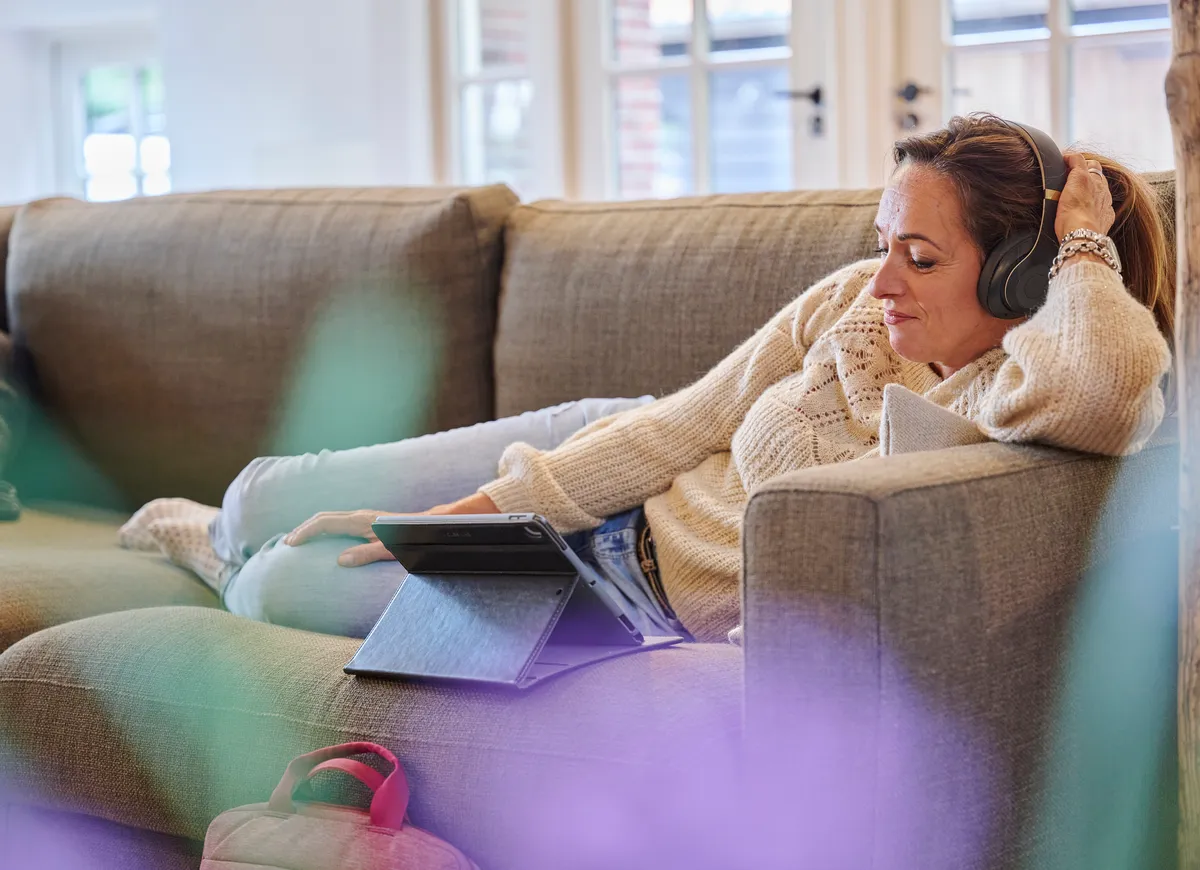 Vrouw met koptelefoon en tablet ligt op de bank