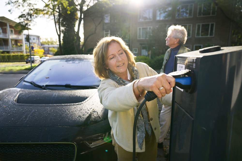 Een stel sluit een elektrische auto aan op een laadpaal om deze op te laden.
