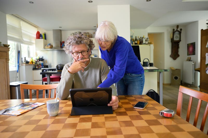 Man en vrouw bekijken scherm van een tablet, terwijl de één staat bij de eettafel en de ander zit.
