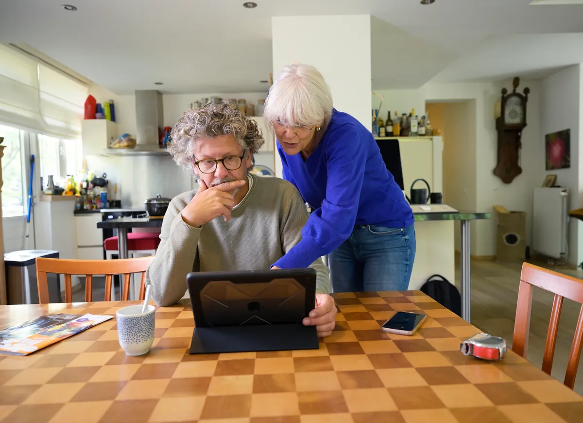 Man en vrouw bekijken scherm van een tablet, terwijl de één staat bij de eettafel en de ander zit.