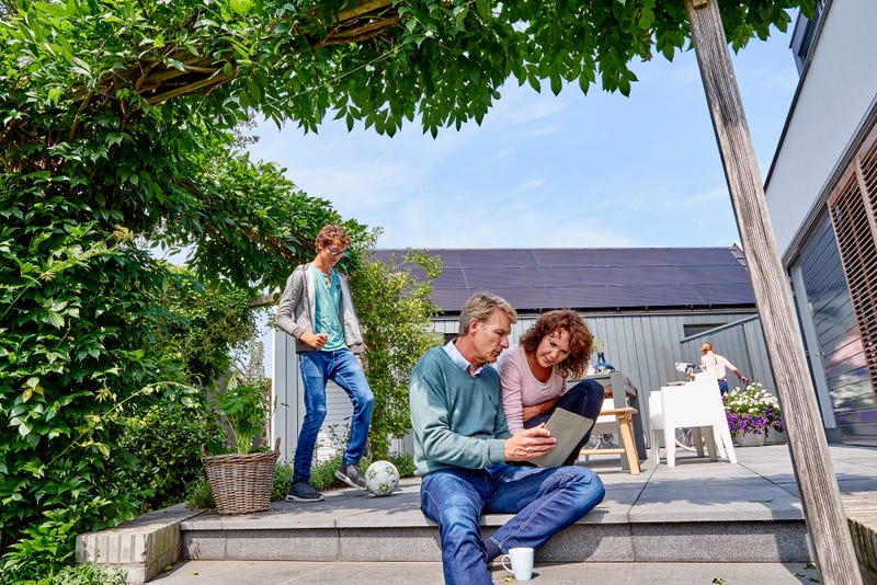 man met tablet in tuin met gezin en zonnepanelen op achtergrond