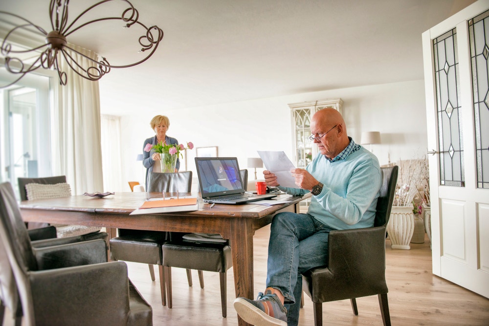 man met papierwerk en laptop aan tafel