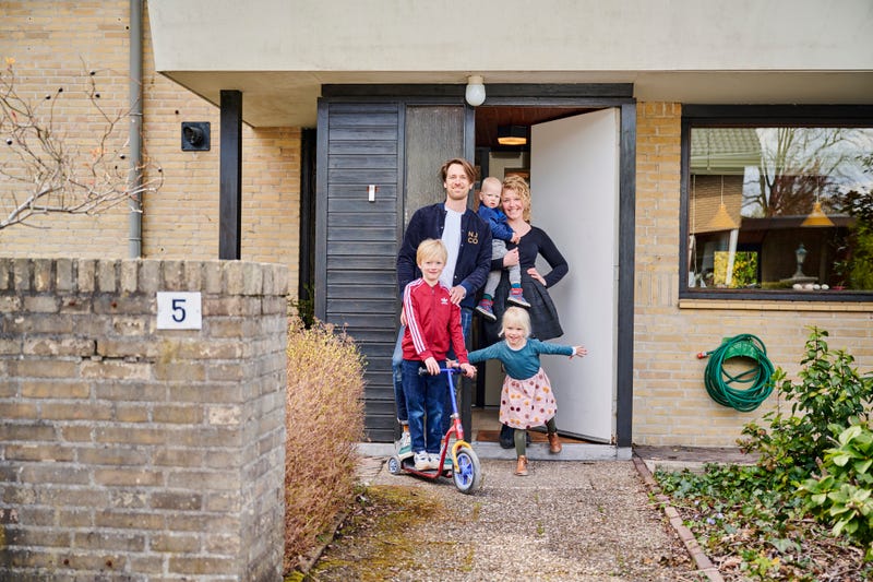 Een man, een vrouw en drie jonge kinderen staan voor de ingang van een huis