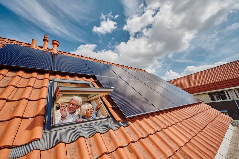 man en vrouw kijken uit dakraam naast zonnepanelen