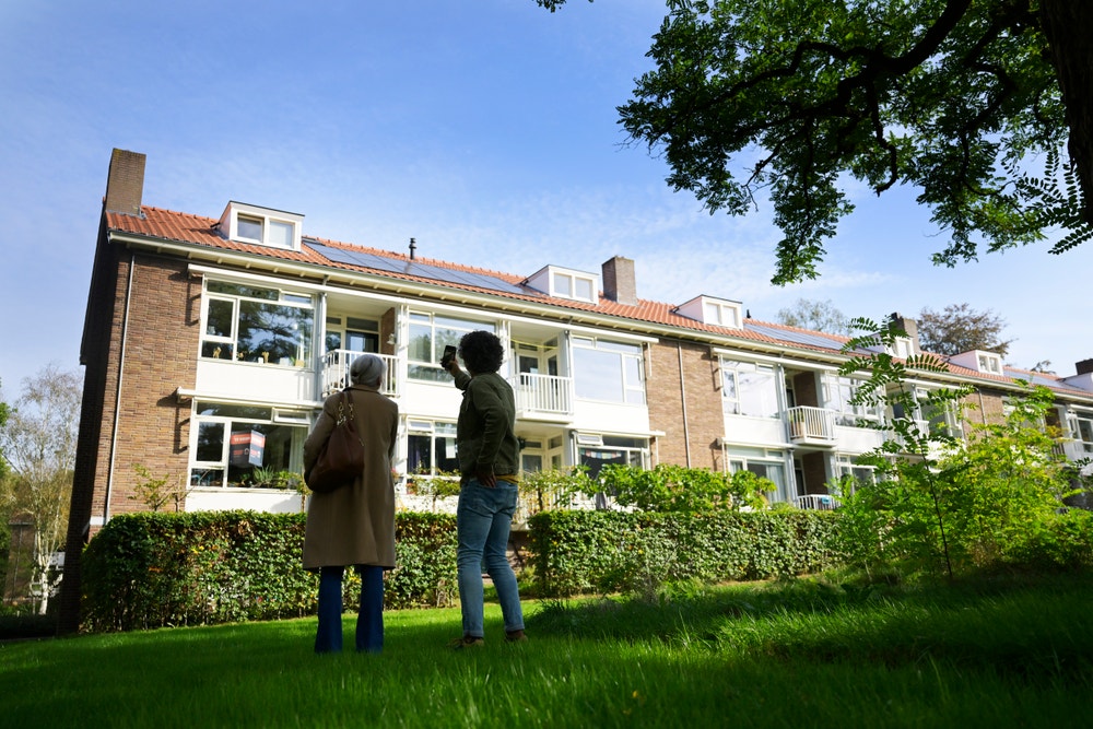 Een stel fotografeert een appartementencomplex met zonnepanelen, omgeven in het groen.
