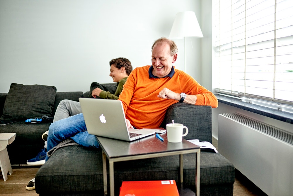 man lachend achter laptop op bank