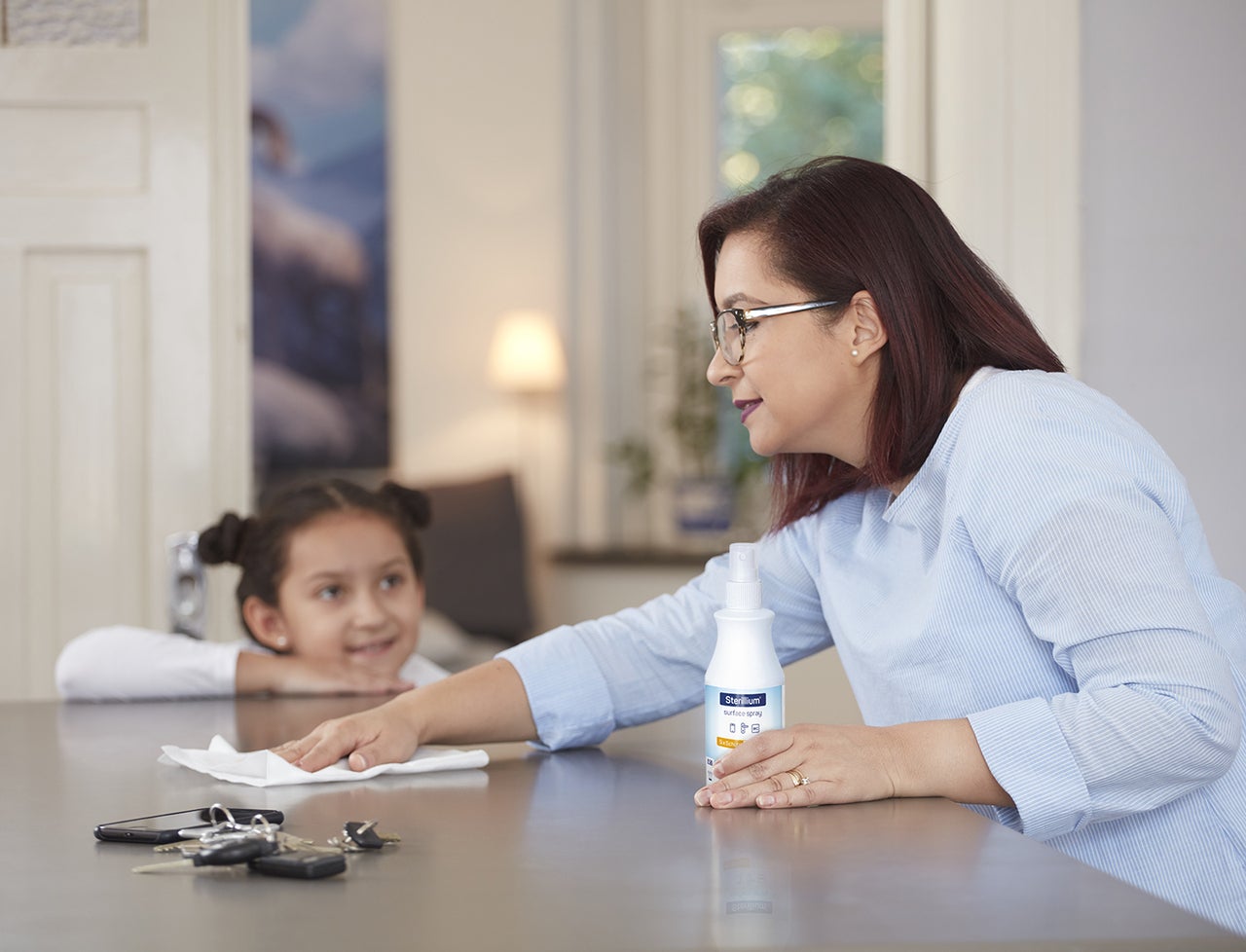 Frau desinfiziert den Tisch mit Sterillium® Surface Spray und Kind schaut zu