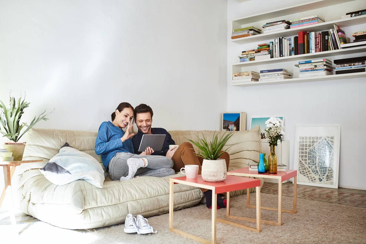 Un jeune couple est assis sur le canapé et regarde un appareil mobile.