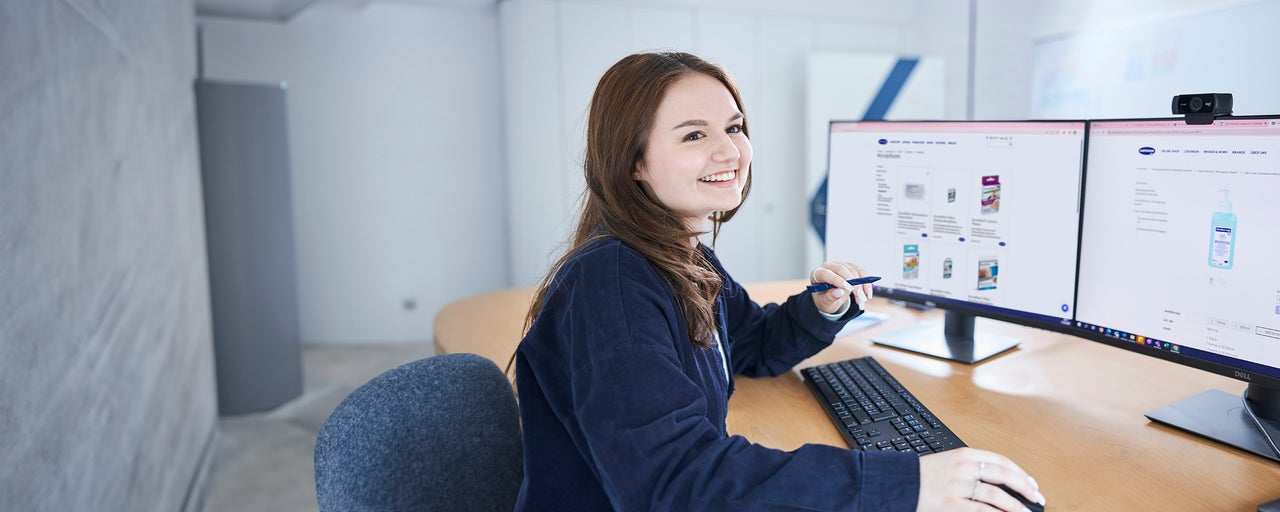 junge frau sitzt vor Bildschirmen am Arbeitsplatz