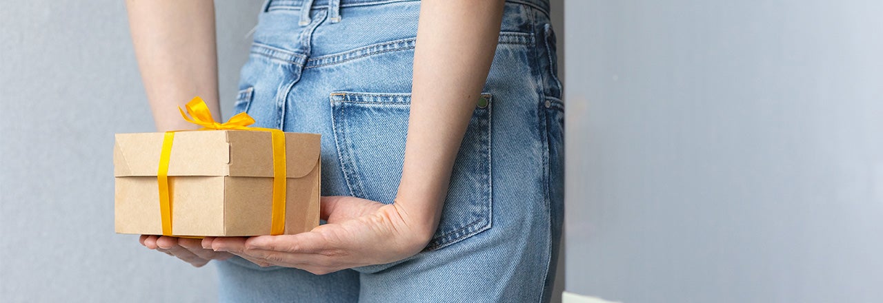 Person hält Geschenk hinter dem Rücken in den Händen