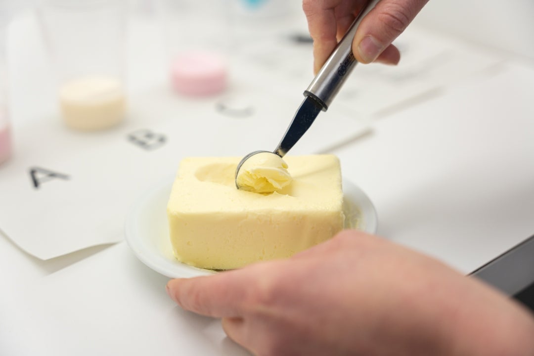 Sensorische Analyse von Butter mit einem kleinen Laborlöffel auf einem weißen Teller.
