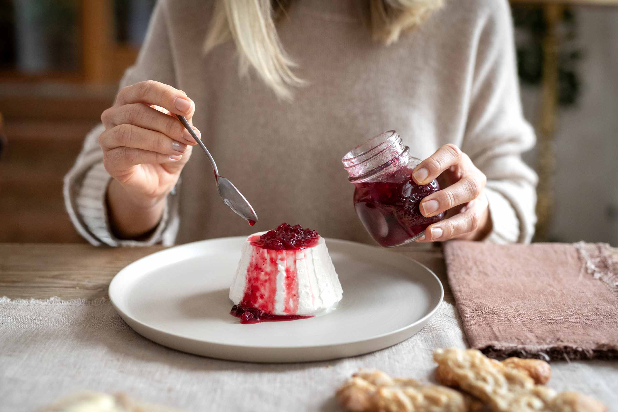 Ricotta mit selbstgemachter roter Marmelade, von einer Frau auf dem Teller angerichtet.