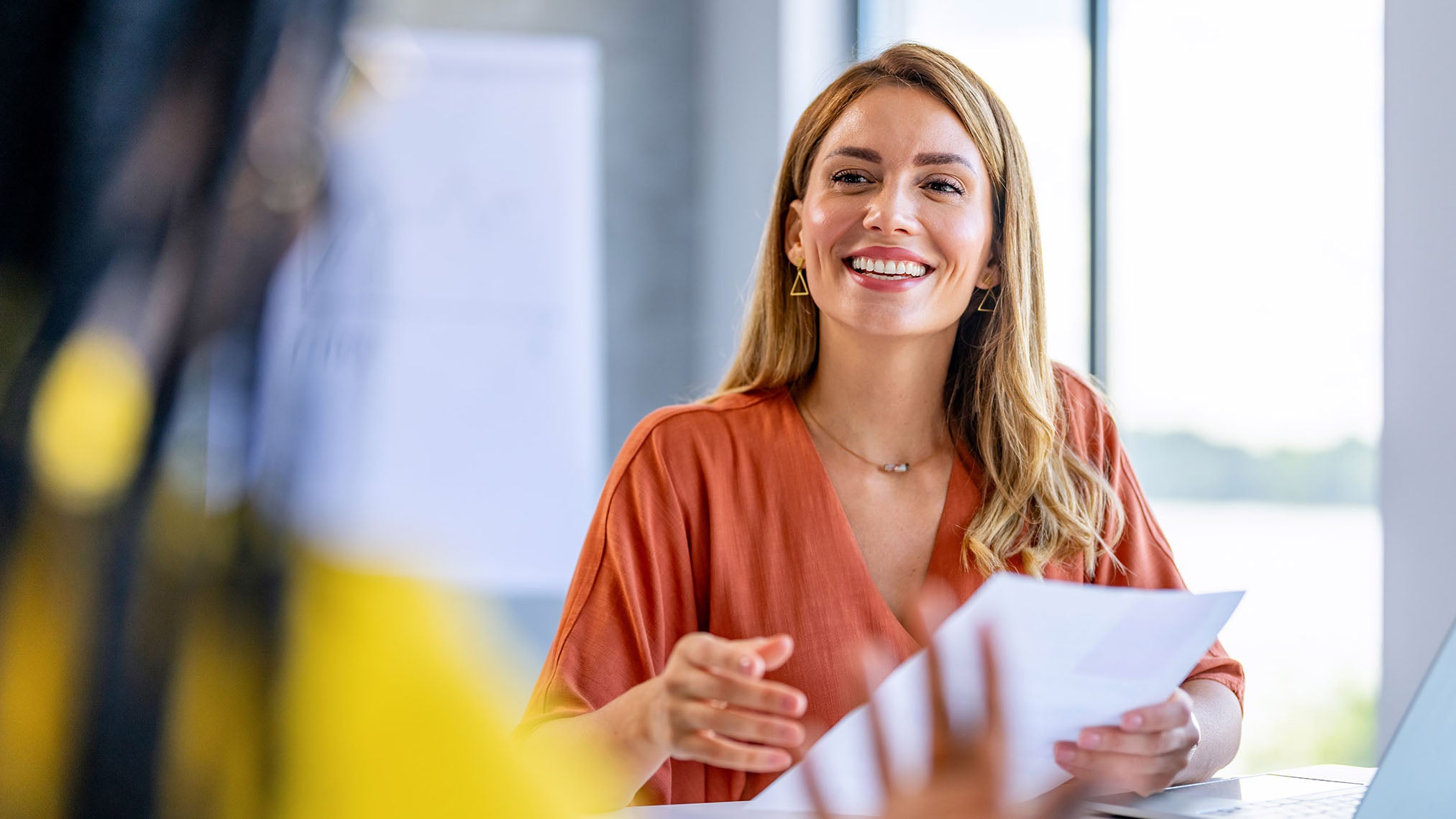 Woman in an orange top holding paperwork