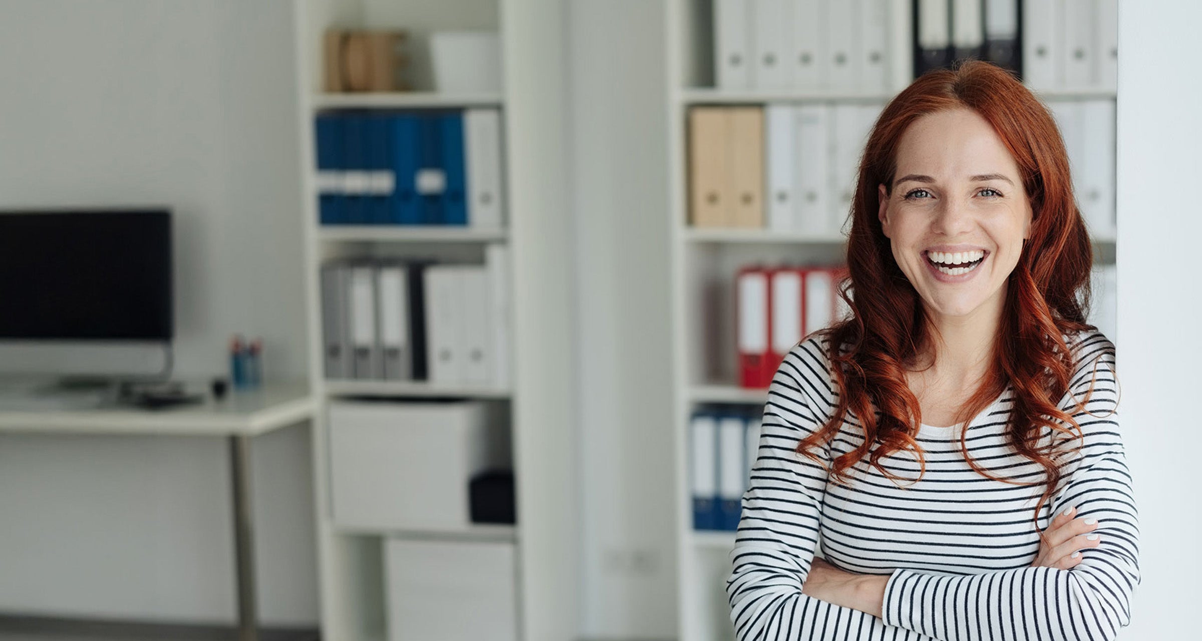 A woman smiling with arms crossed in a bright top