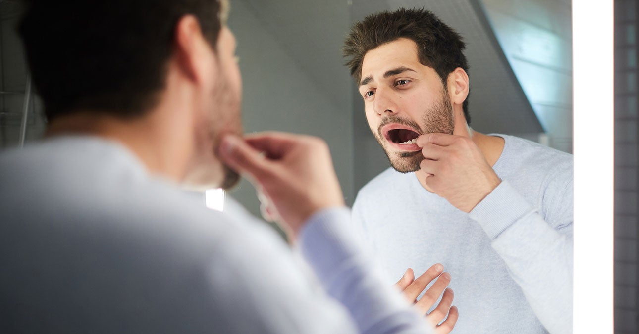 Man looking at this teeth in front of a mirror