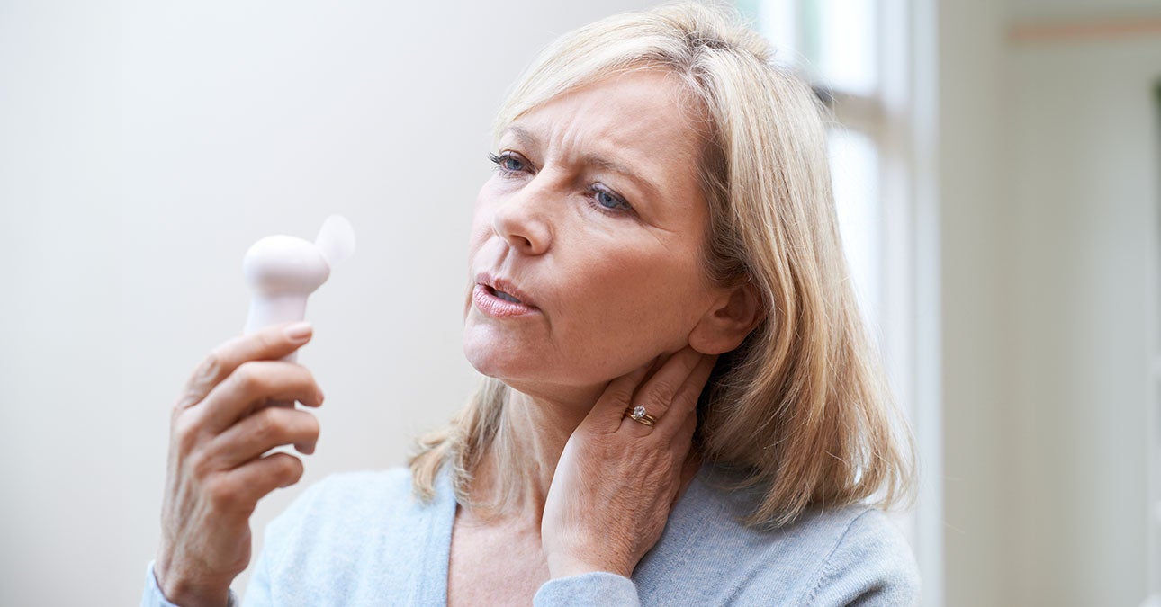 A woman feeling unwell using a small fan to cool down