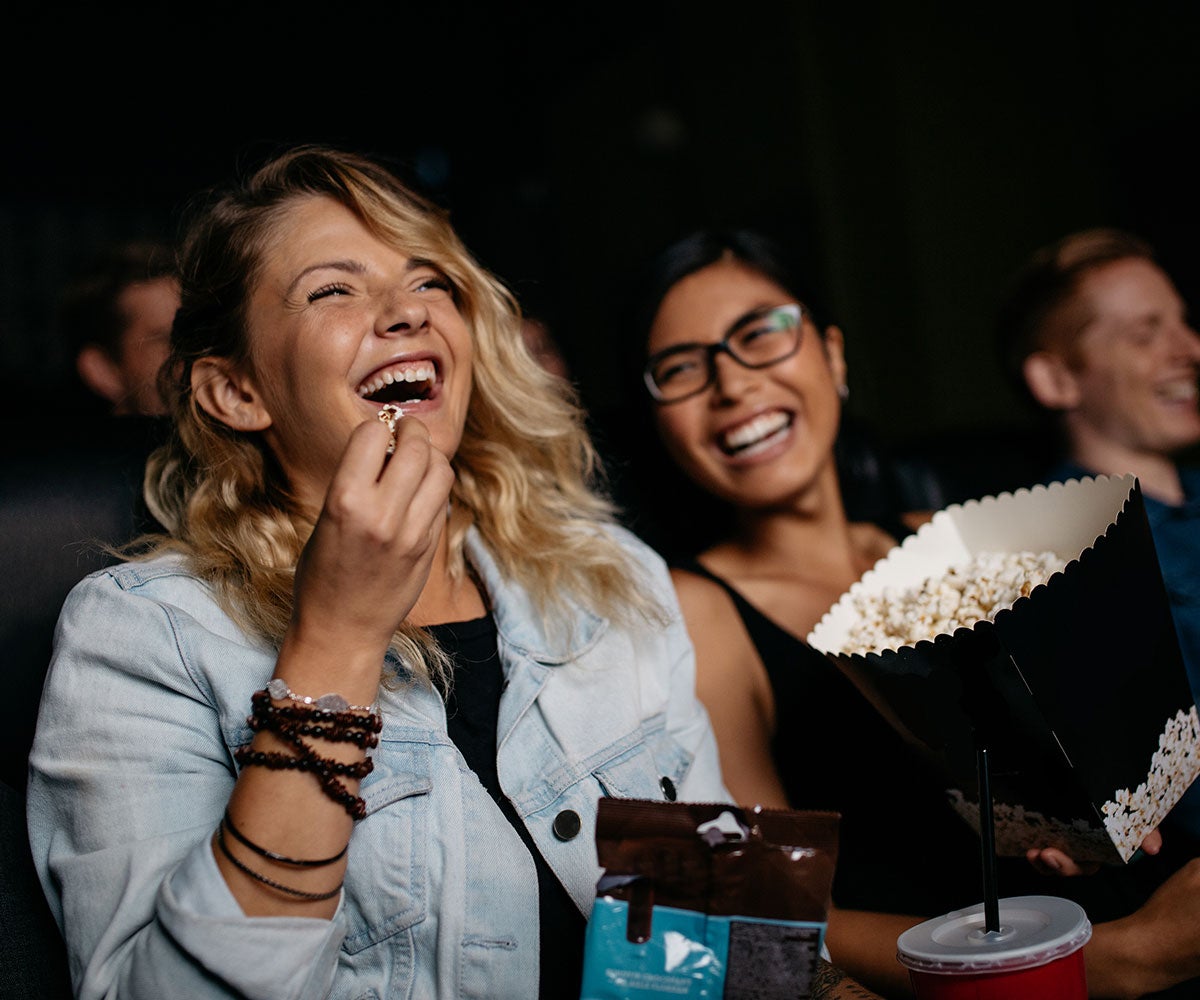 Happy girls laughing and eating popcorn watching a movie