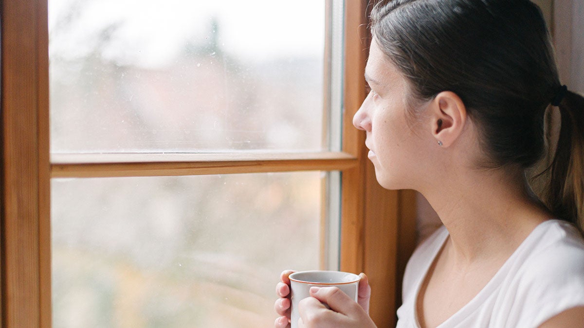 Woman looking through the window drinking tea