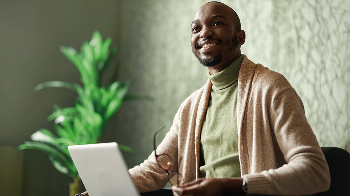 A man smiling while holding a laptop