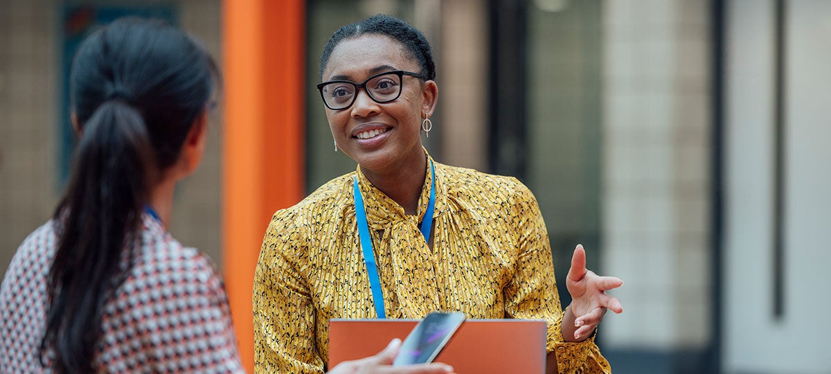 Lady with a yellow top and blue lanyard having a discussion with a person in the office environment.