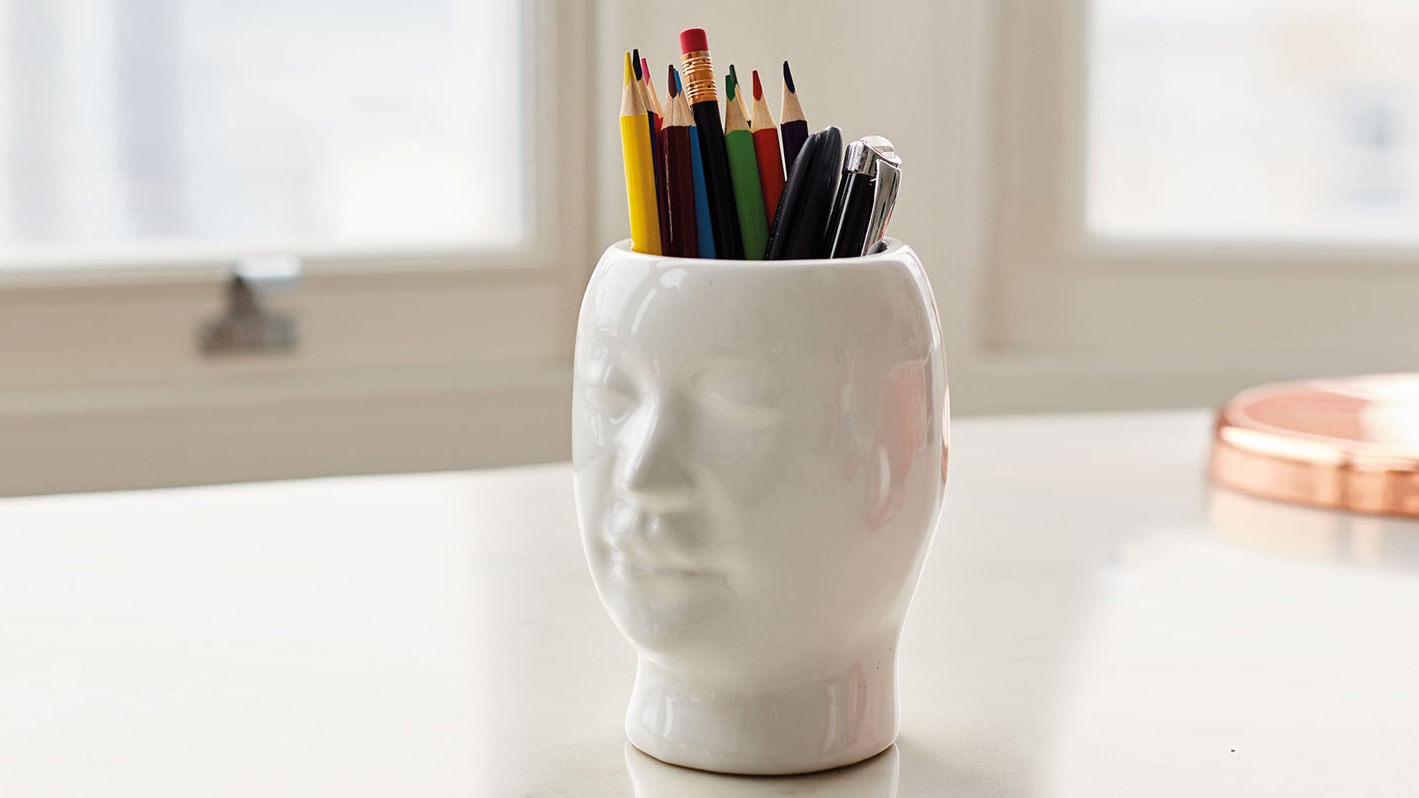 White cup in the shape of a head with pencils in it.