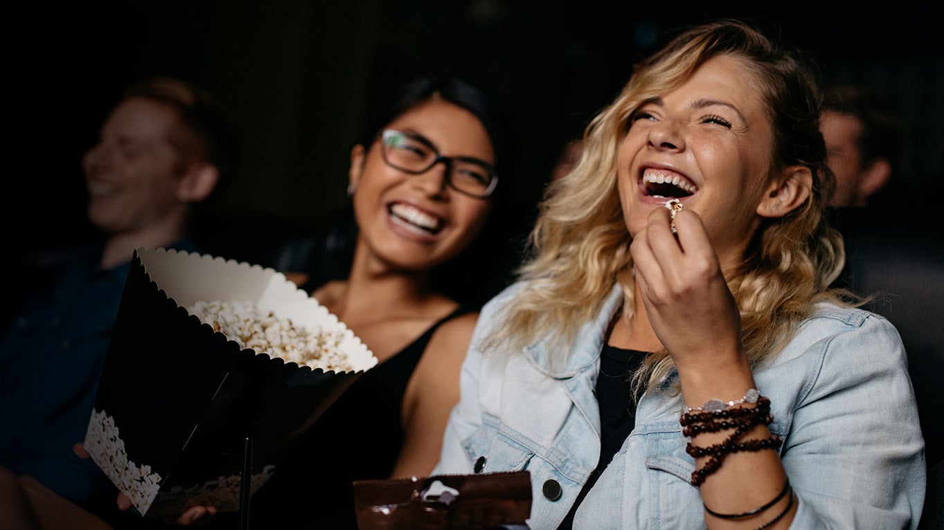 Happy girls laughing and eating popcorn watching a movie
