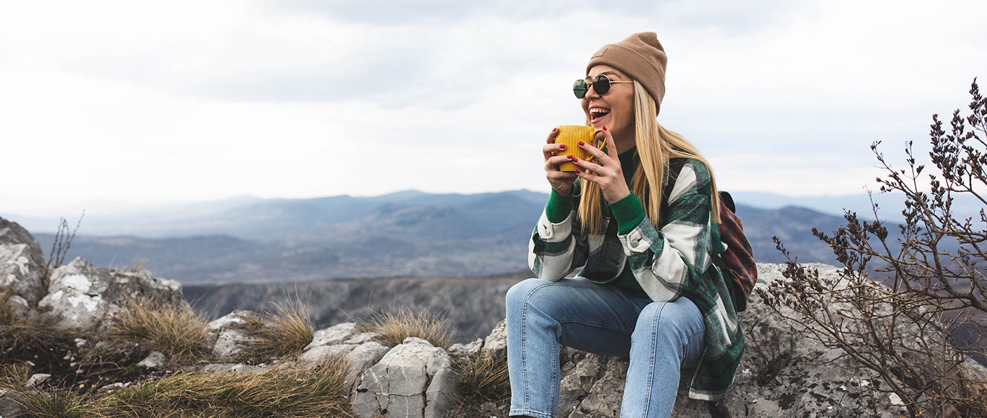 A woman sitting on a rock holding a yellow cup