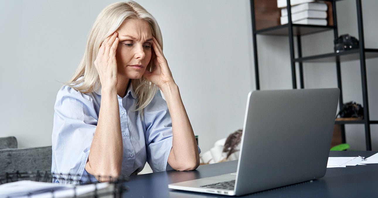 Woman holding her head struggling to focus on her work sitting in from of a laptop