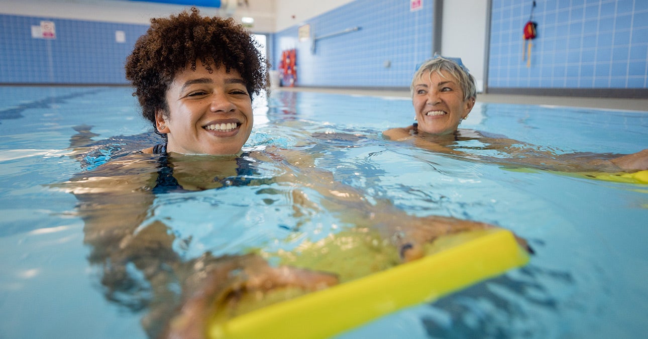 Two smiling women swim in an indoor pool with yellow floats, doing an activity to promote their wellness and reduce the impact of their long-term conditions, something Unum can help with for working people with a Wellness Action Plan.