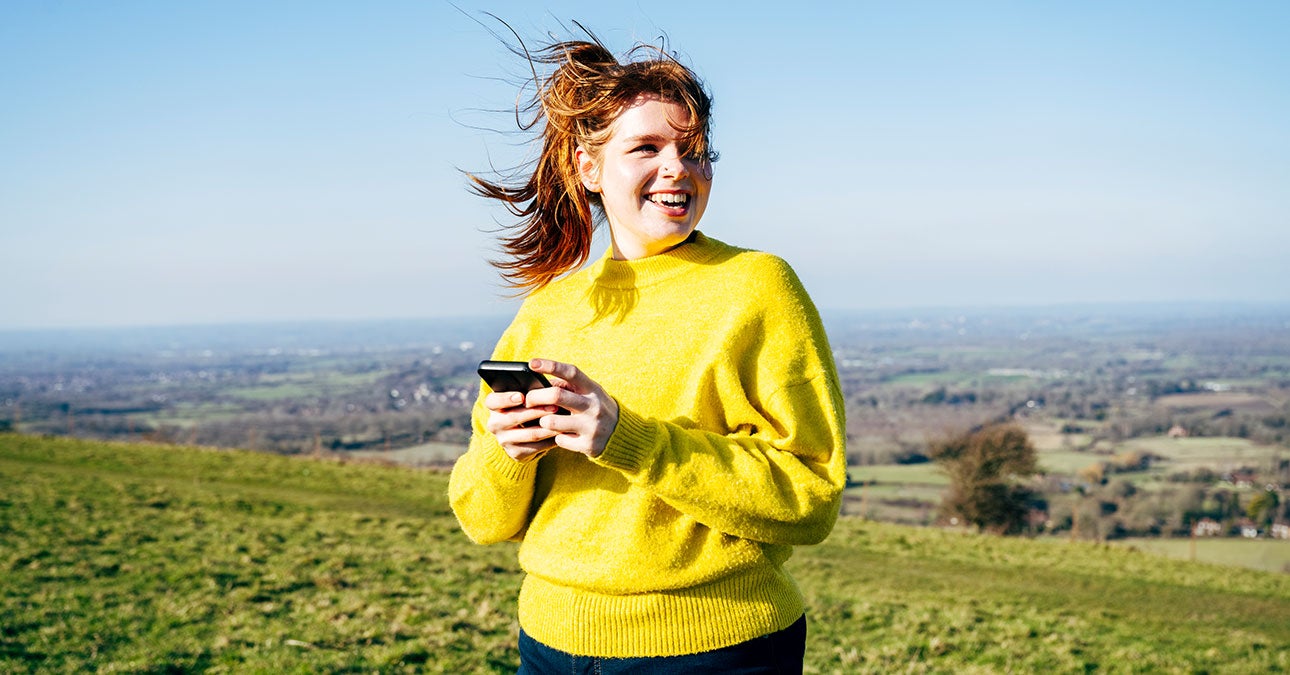 Happy woman in yellow jumper walking outdoors using her phone