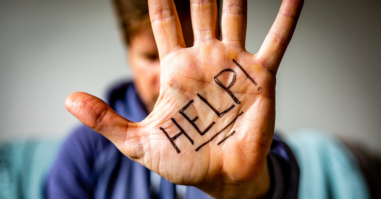 A person, head bowed, extends their left hand towards the camera, palm towards us. On the palm, the world "Help" is written in big bold black letters, emphasised by an exclamation mark at the end and two lines beneath.