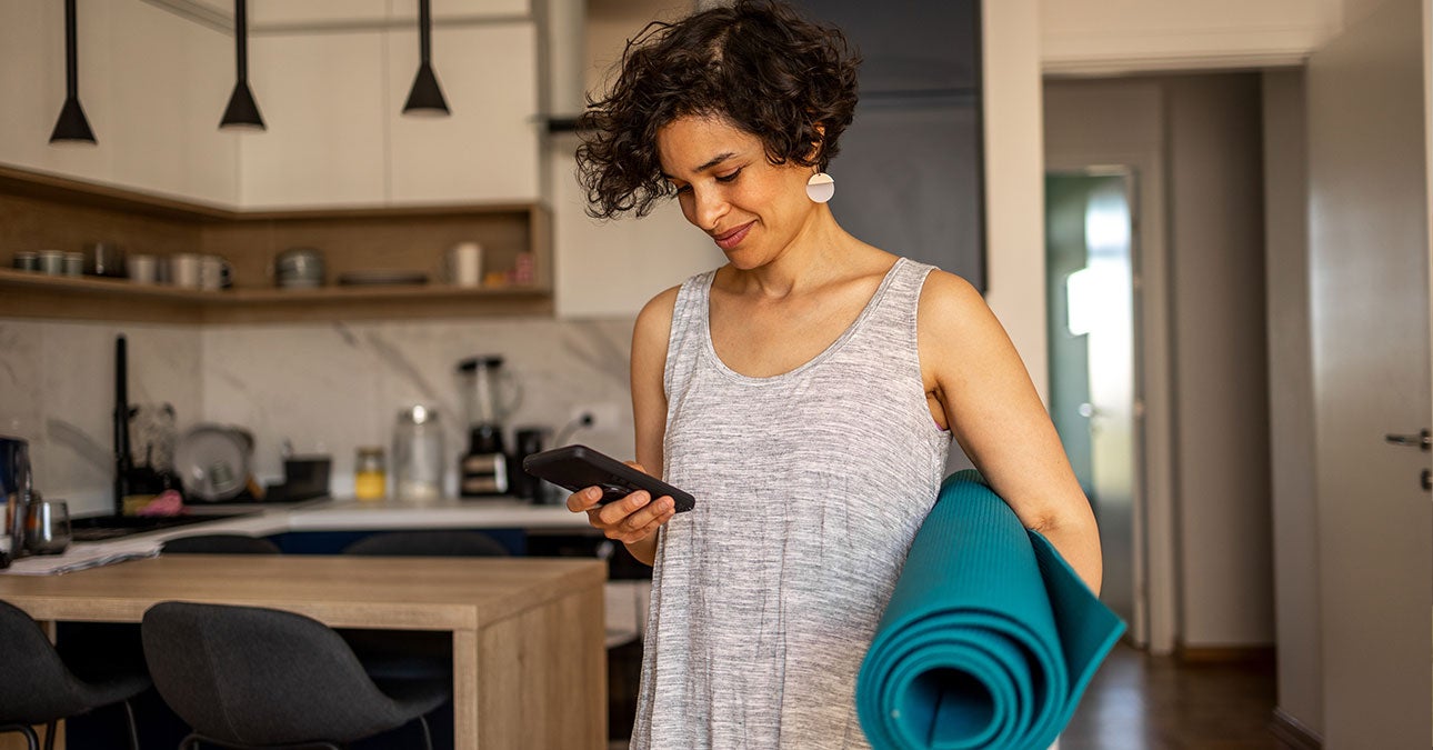 Woman holding her yoga mat scrolling through Unum's wellbeing resources