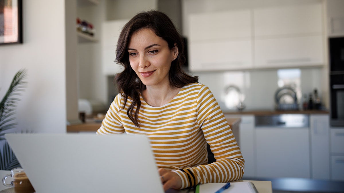 Woman on a laptop sitting at the dining room table in home environment 