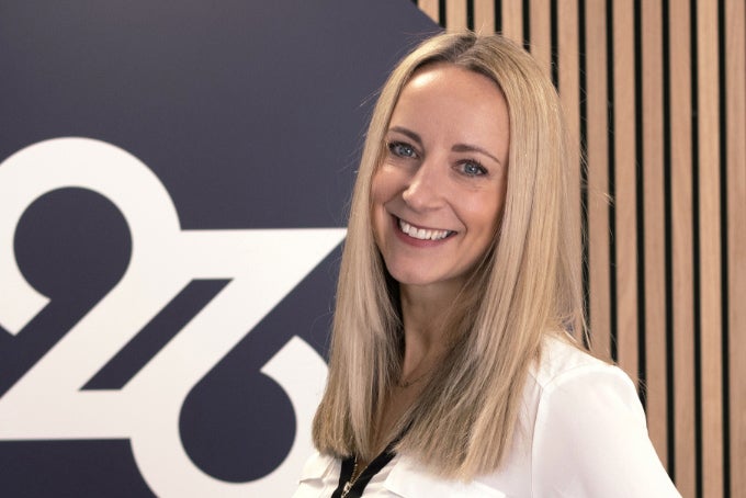 Headshot of Ellie Foxton-Brown, with the 26 logo in the background.