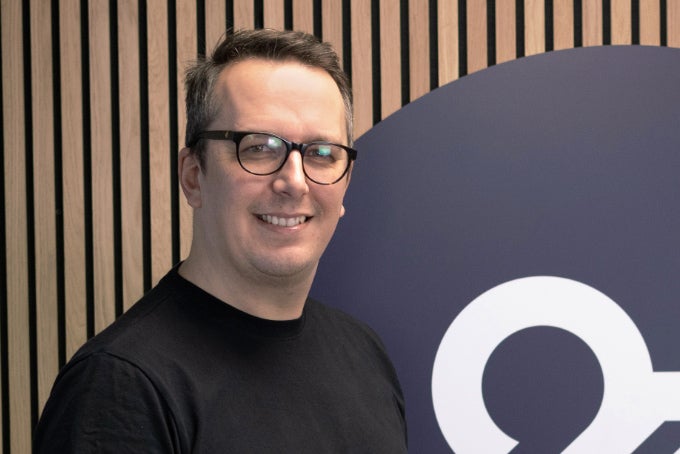 Headshot of Ryan Scott, with the 26 logo in the background.